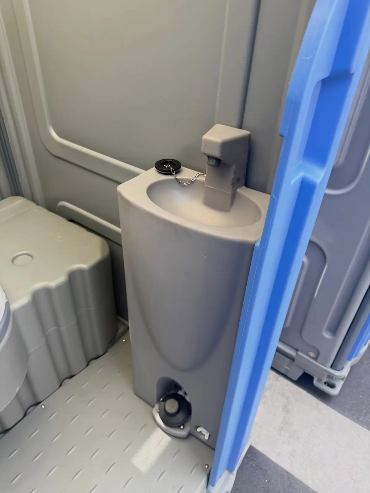Inside a flushing porta potty with a foot-pump hand sink beside the toilet