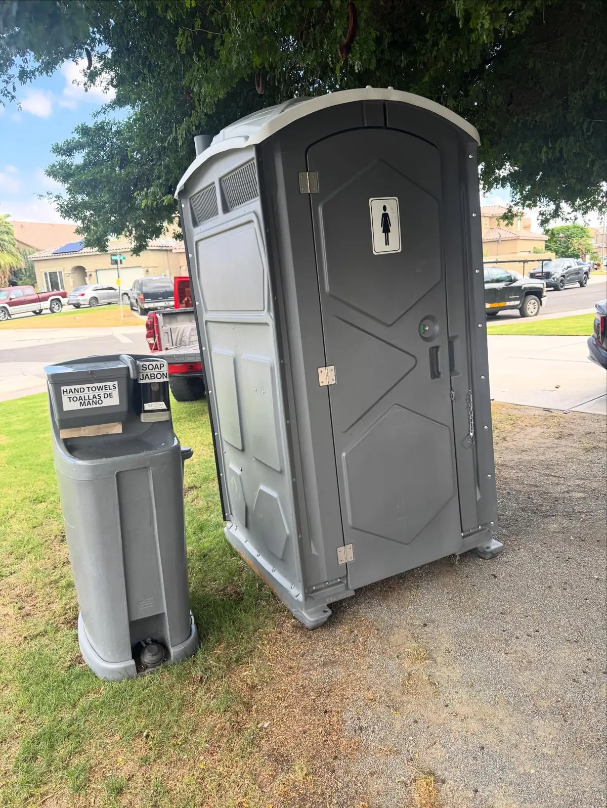 Gray portable toilet and a handwashing station on a lawn