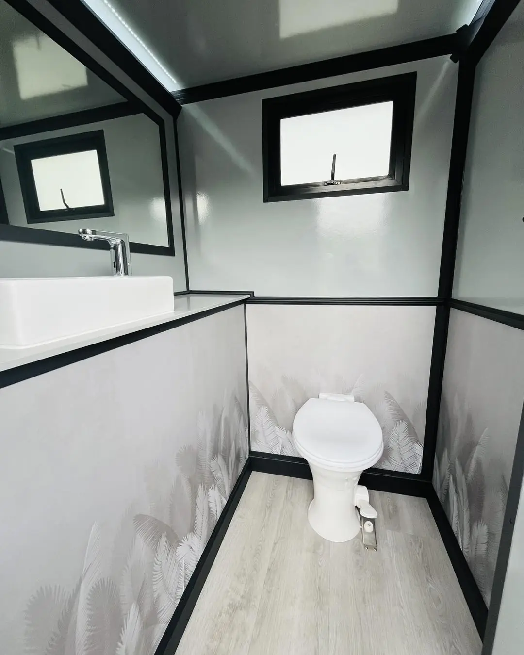 Inside a restroom trailer stall with a vanity sink, mirror and flush toilet