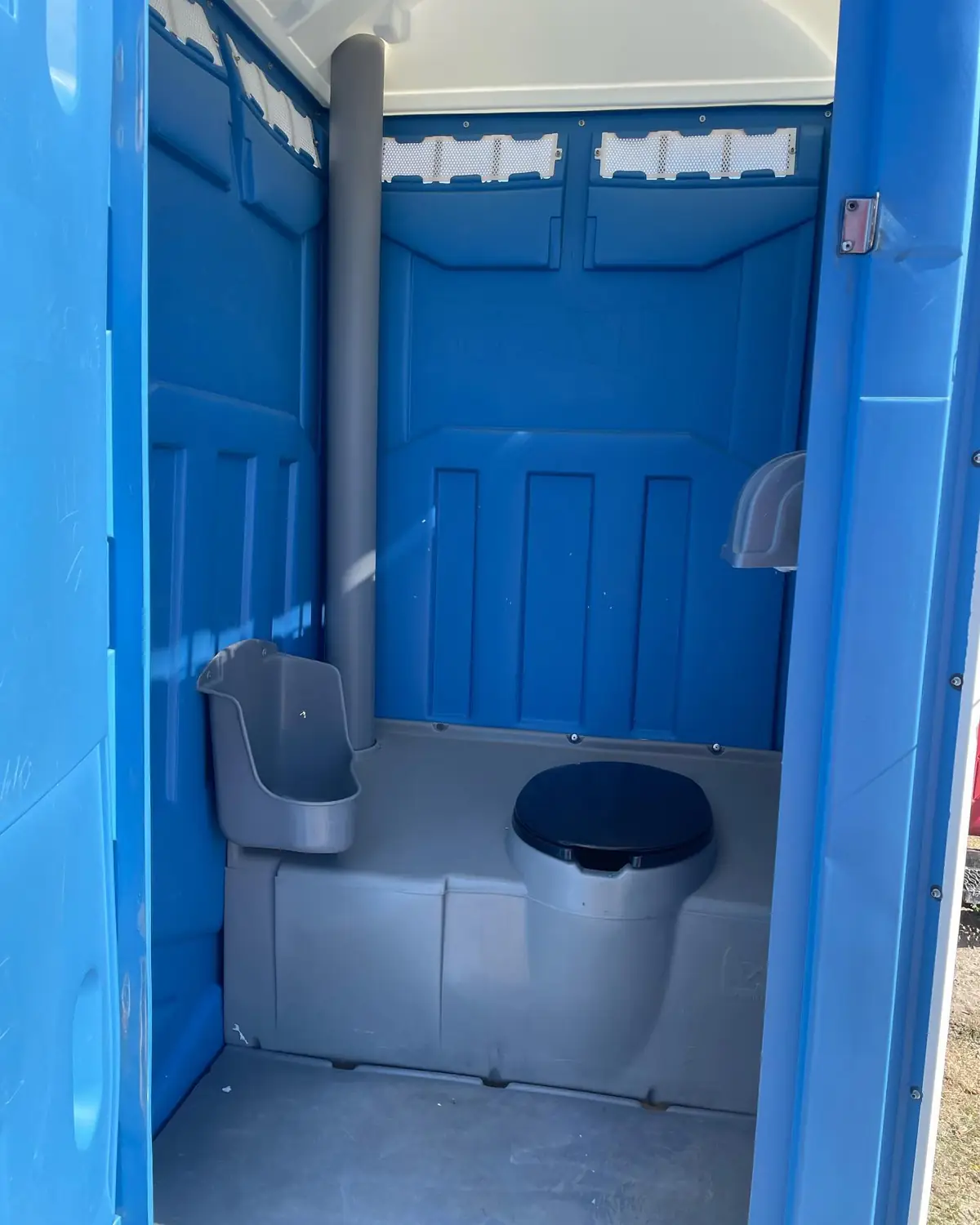 Interior of a blue standard porta potty showing the seat, urinal and vent pipe